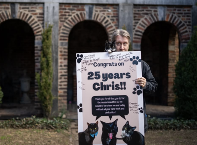 Person holding Tib the kitten and a sign that says Congrats on 25 years Chris!